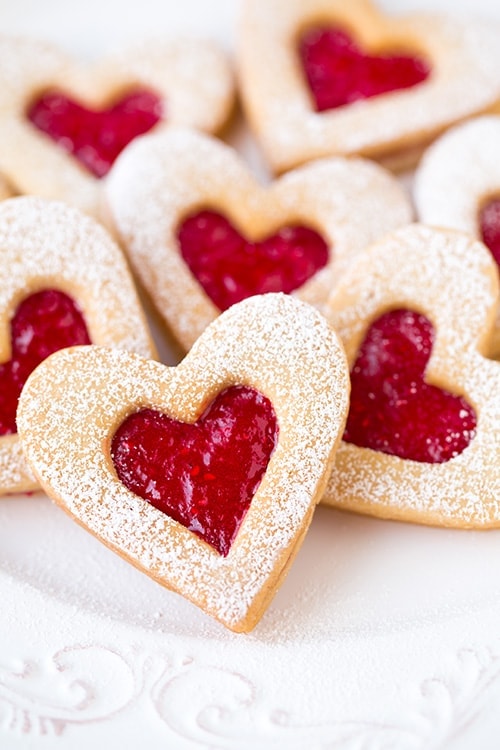 A close up shot of heart shaped linzer cookies with red middles and powdered sugar on the outside.
