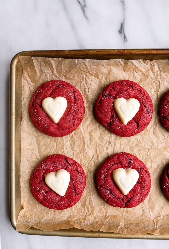 Above image of red velvet sugar cookies with hearts on top on a baking pan.