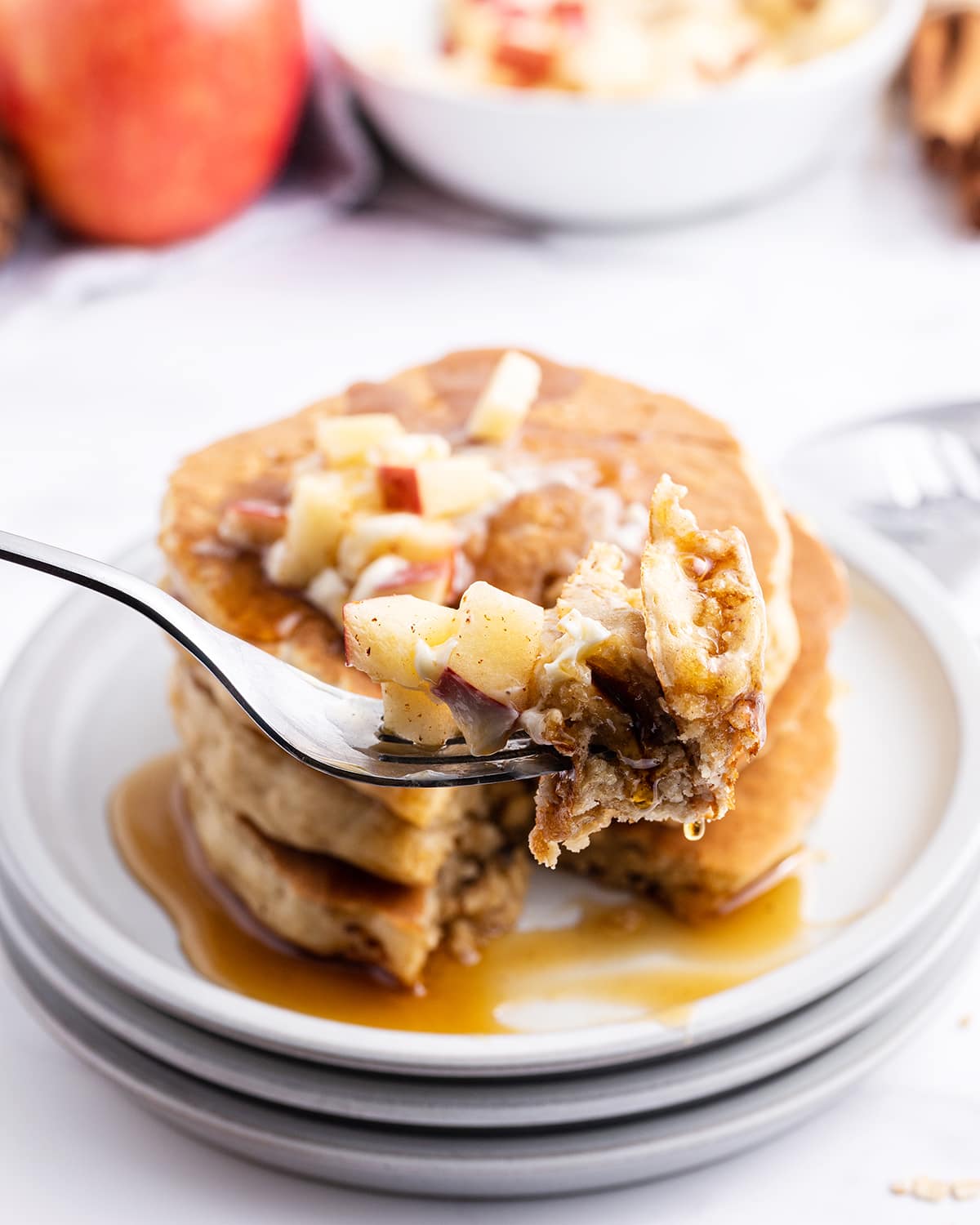 A bite of applesauce pancakes on a fork in front of a stack of pancakes.