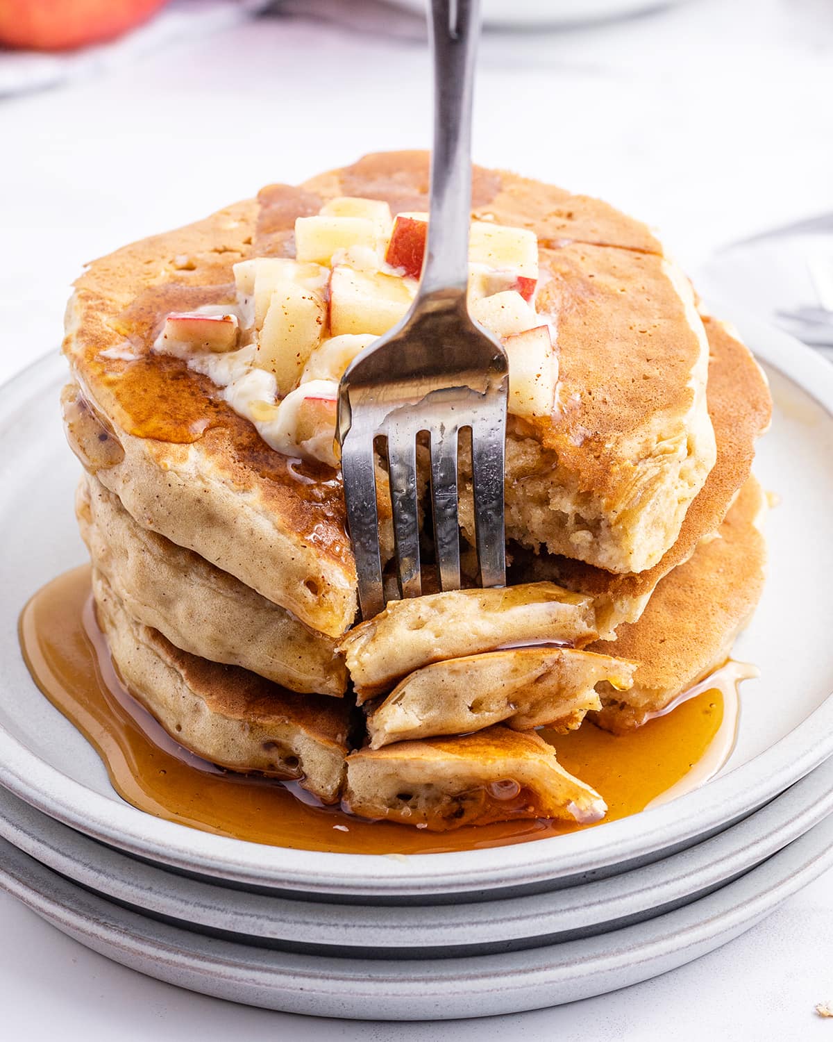 A close up of a stack of applesauce pancakes with a forkful being stuck with a fork.