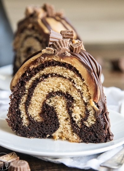 A piece of chocolate peanut butter swirled bundt cake topped with ganache and peanut butter cups on a plate.