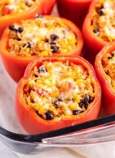 Mexican stuffed peppers topped with shredded cheese in a baking dish.