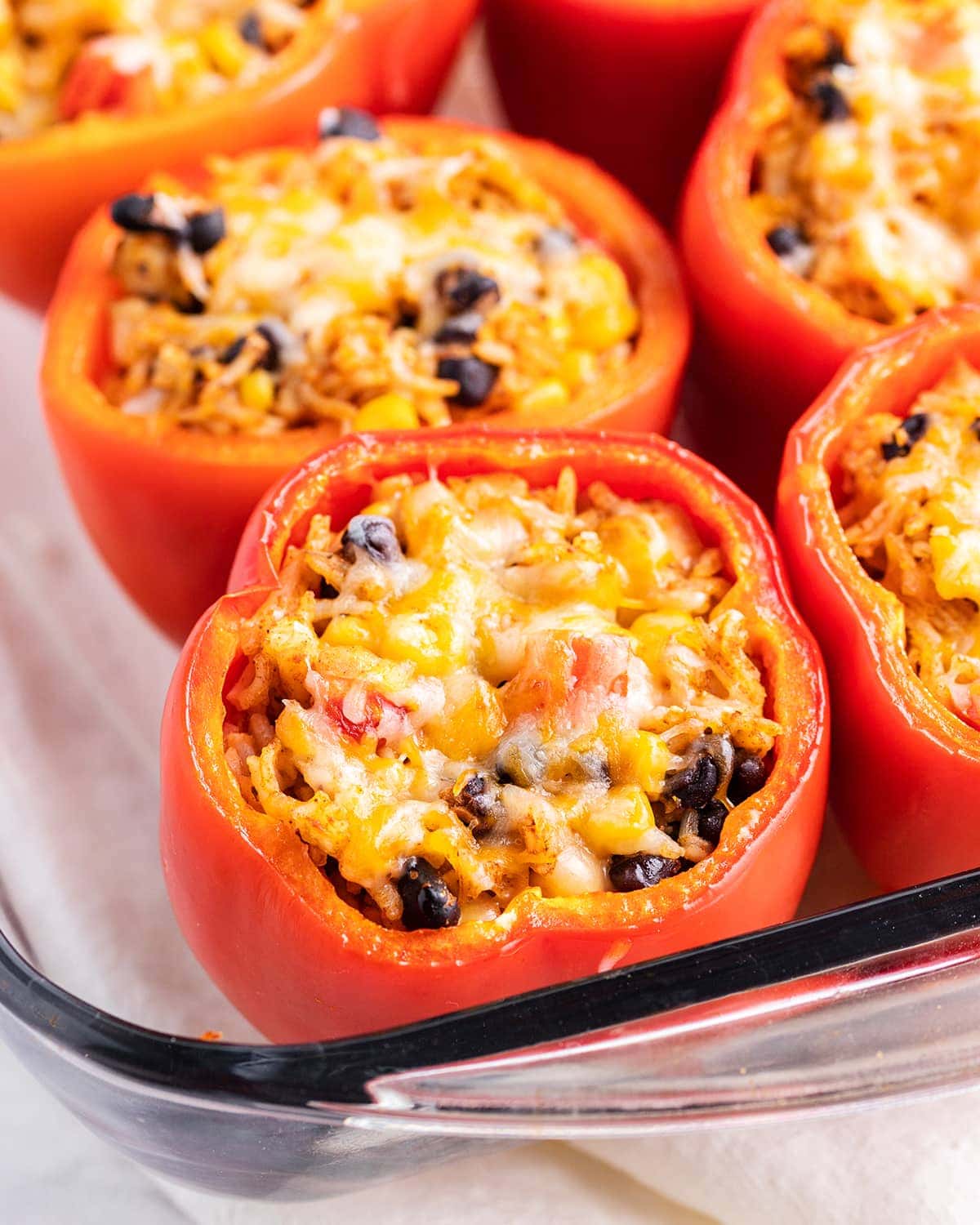Mexican stuffed peppers topped with shredded cheese in a baking dish.