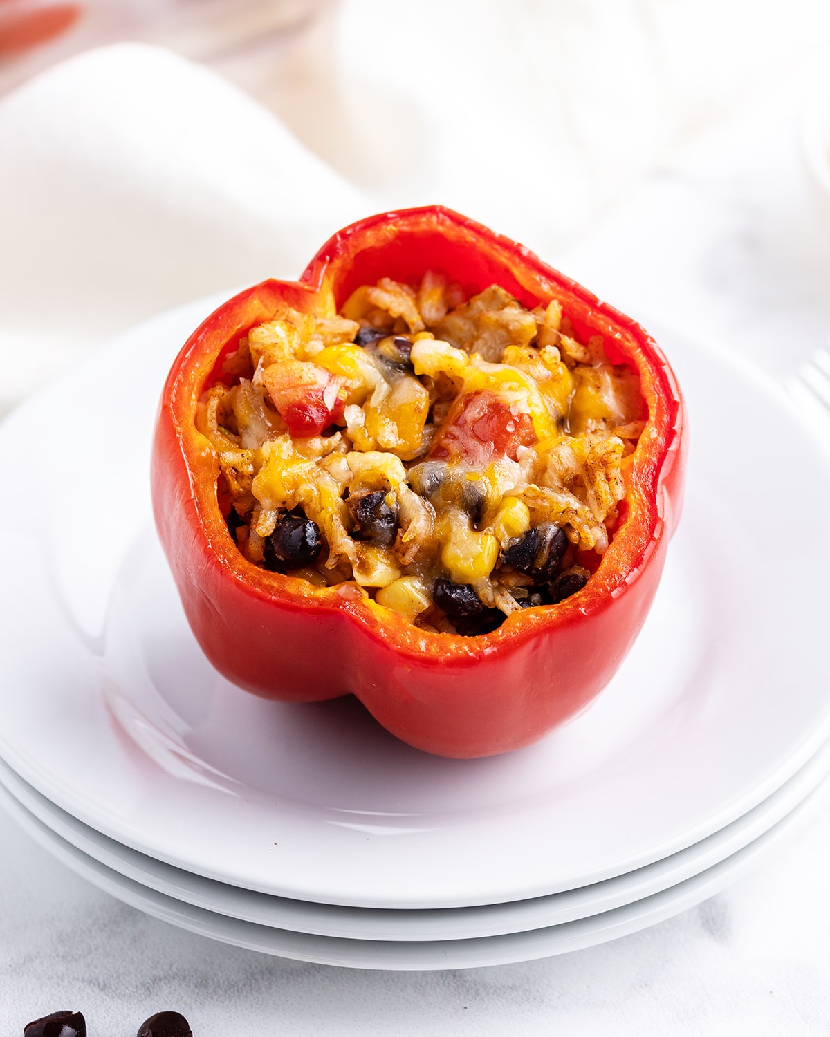 A stuffed pepper topped with melted cheese on a stack of white plates.