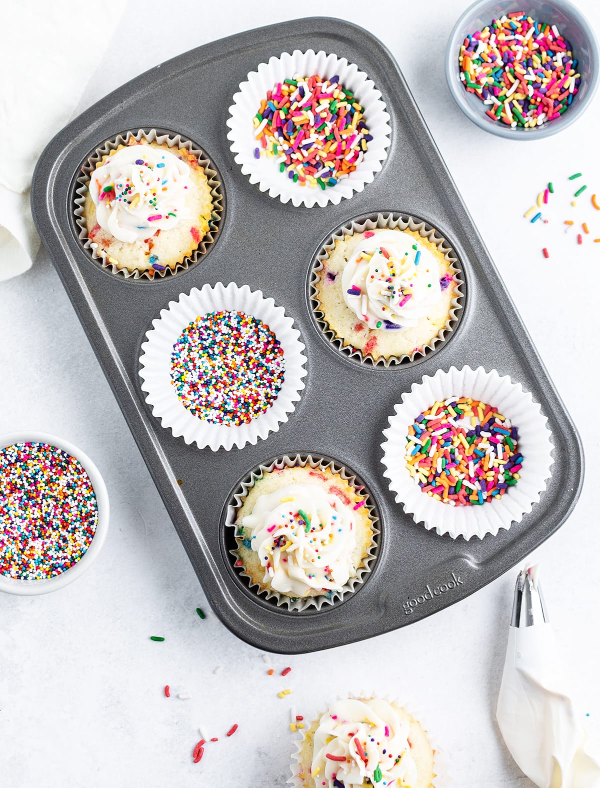 An overhead photo of three cupcakes in a small muffin tin, with sprinkles, and a cupcake on the side.