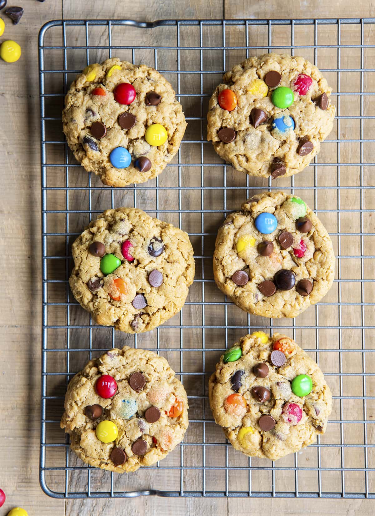 An overhead photo of six monster cookies topped with m&ms on a wire ocoling rack.