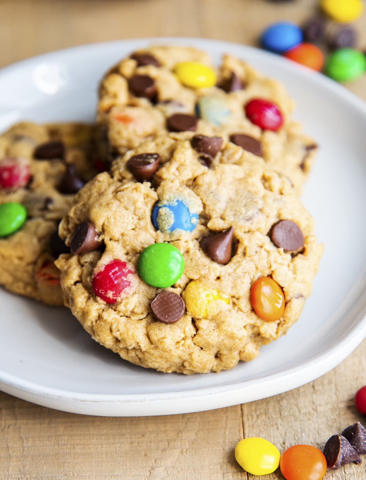 Three monster cookies with chocolate chips and m&ms on a plate.