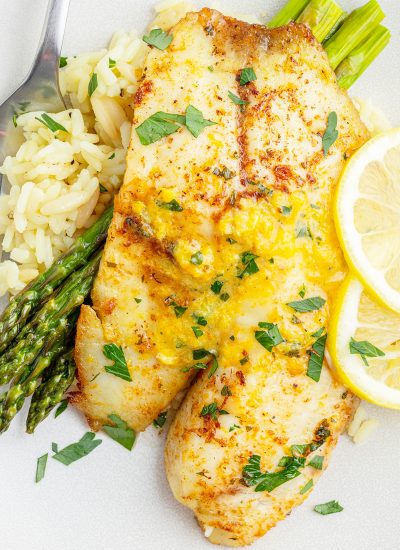 A close up of a tilapia filet topped with a pat of citrus butter and fresh mint on a pile of rice and asparagus.