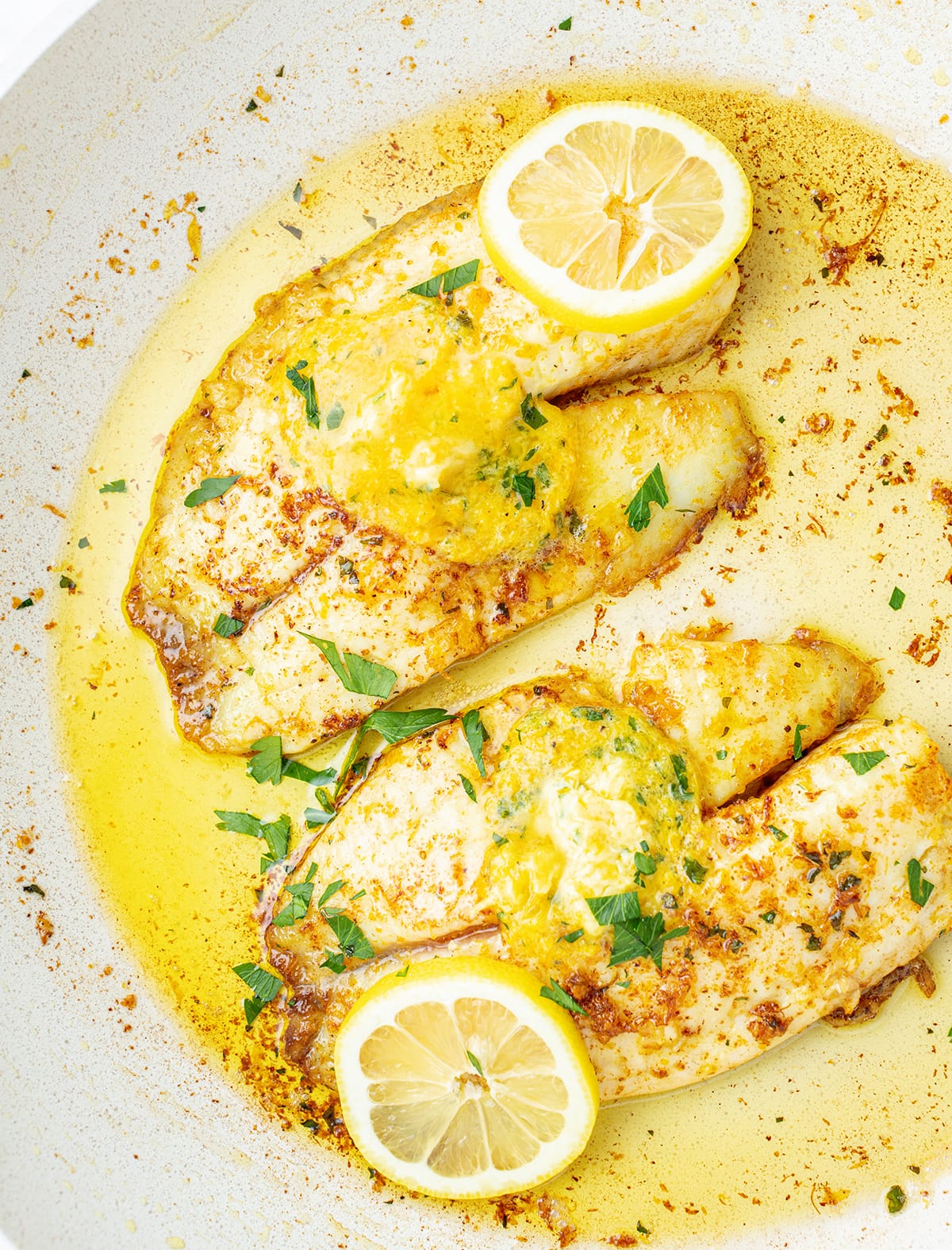 Two Tilapia fillets topped with citrus butter and lemon slices.