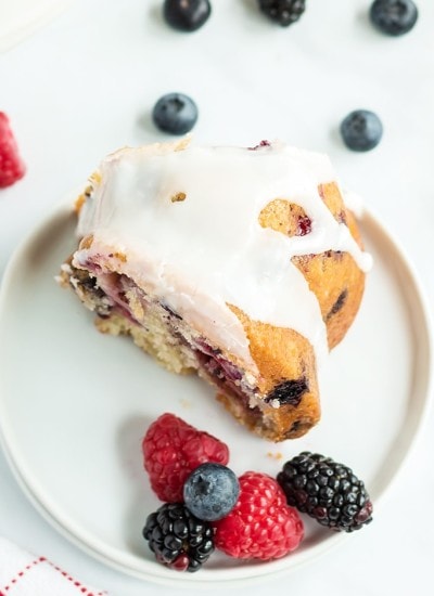 A slice of lemon berry bundt cake with lemon glaze on top on a white plate