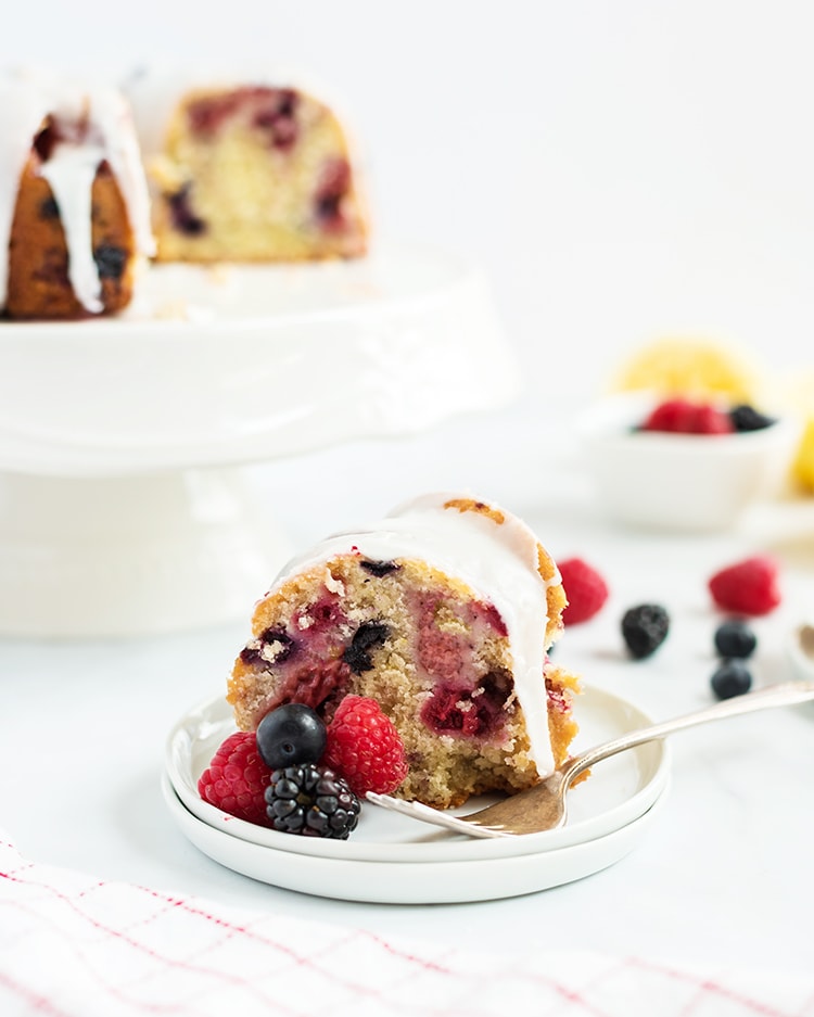 A slice of lemon berry bundt cake with lemon glaze on top on a white plate