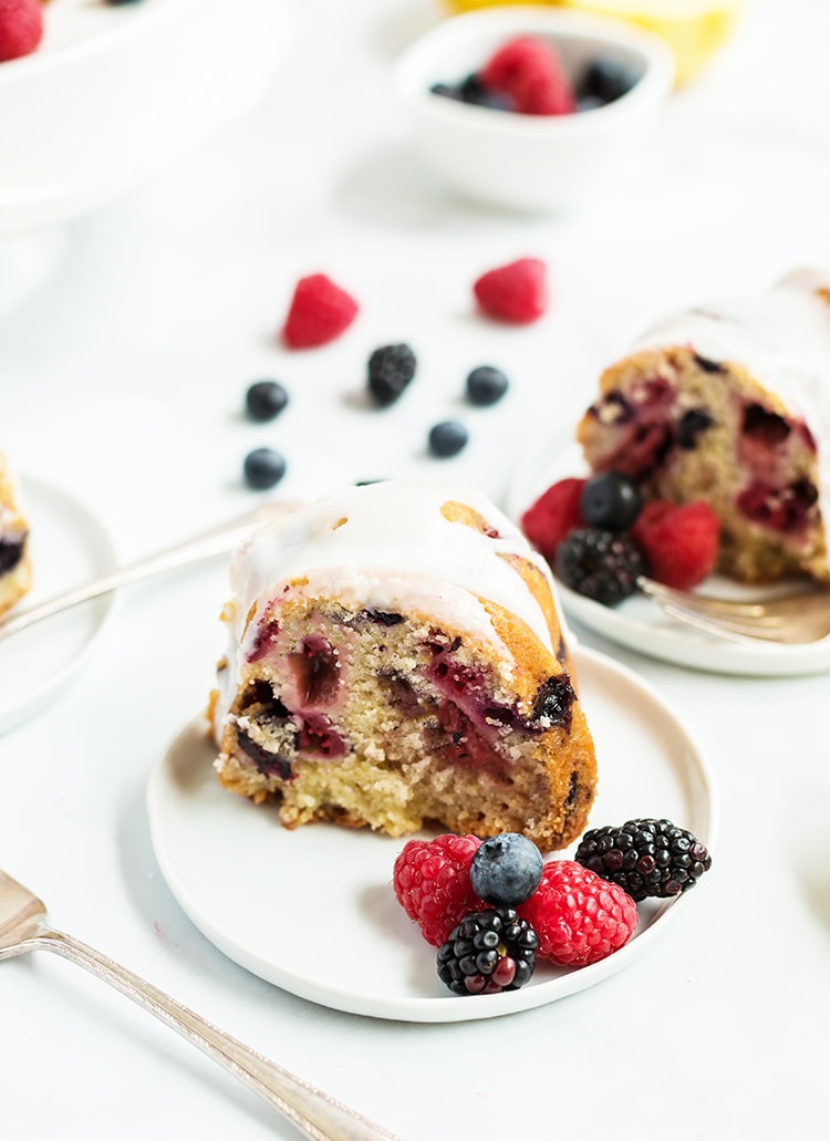 A slice of lemon berry bundt cake with lemon glaze on top on a white plate