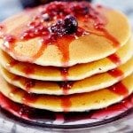Angled view of a stack of pancakes with berry syrup on a plate.
