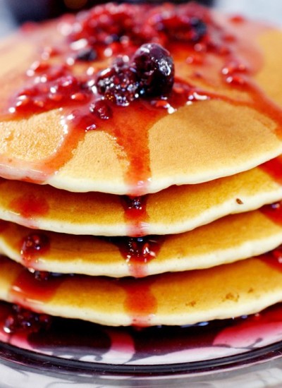 Angled view of a stack of pancakes with berry syrup on a plate.