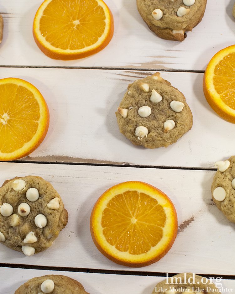 Top view of creamsicle cookies stacked on a white wooden board with orange slices.