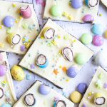 A spread of chocolate bark, topped with white chocolate, covered in chopped up malted eggs, m&ms, and pastel sprinkles.