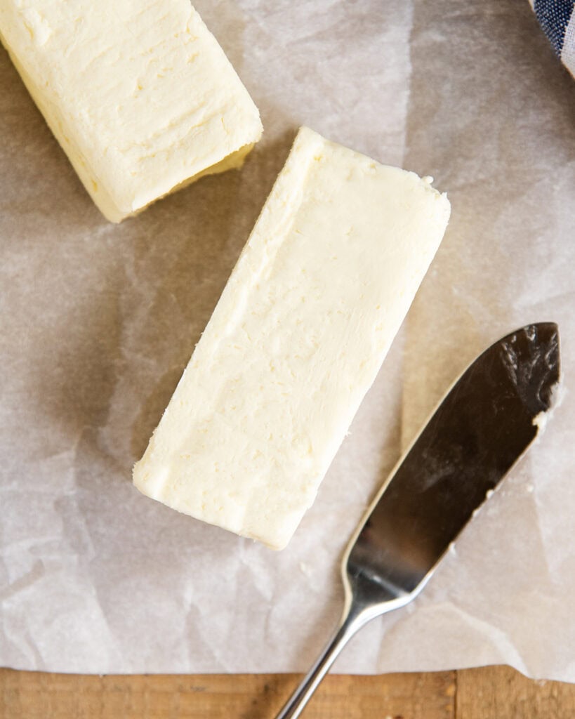 An above view of a stick of butter on a piece of parchment paper, with a spreading knife next to it.