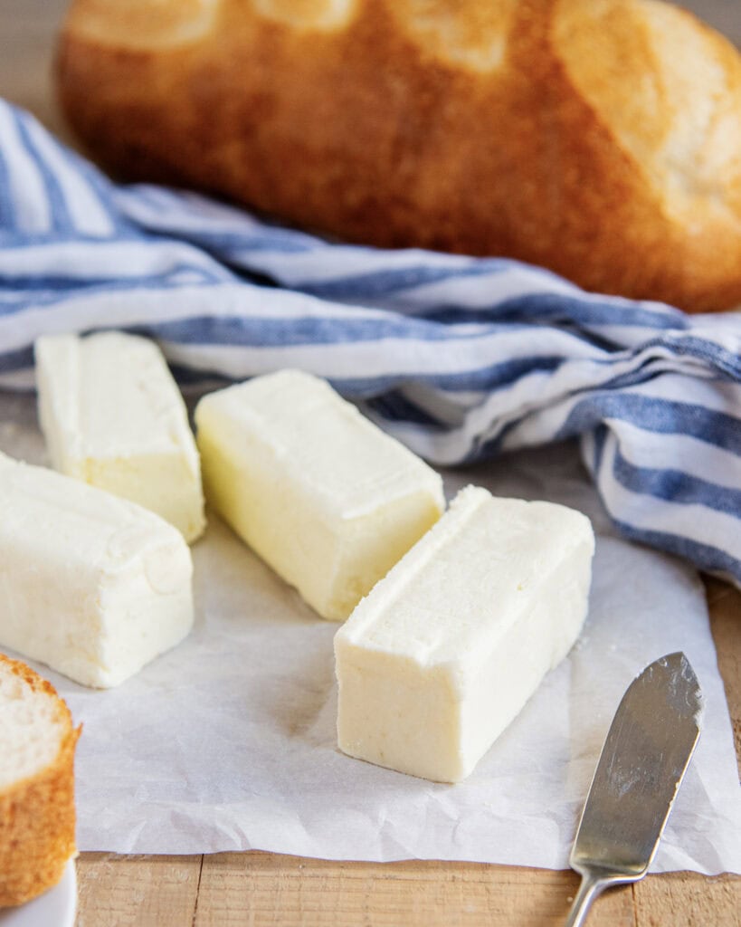 Butter sticks on a piece of parchment paper with a loaf of bread behind them.