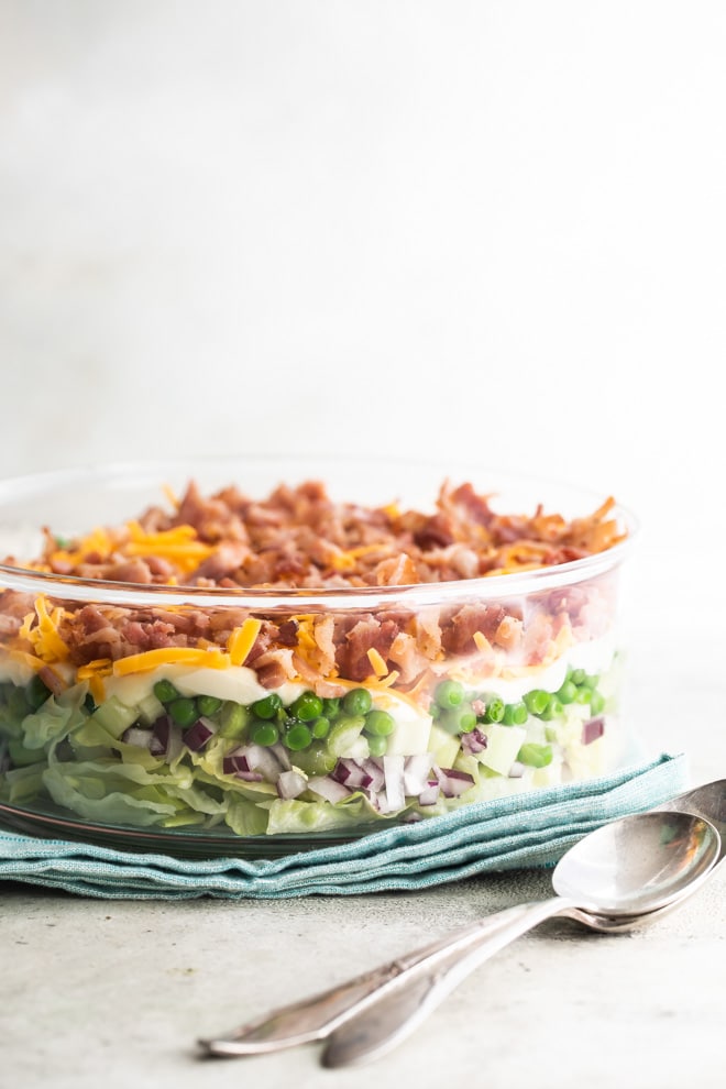 A 7 layer salad in a clear bowl so you can see all the layers including lettuce, peas, bacon, and cheese.