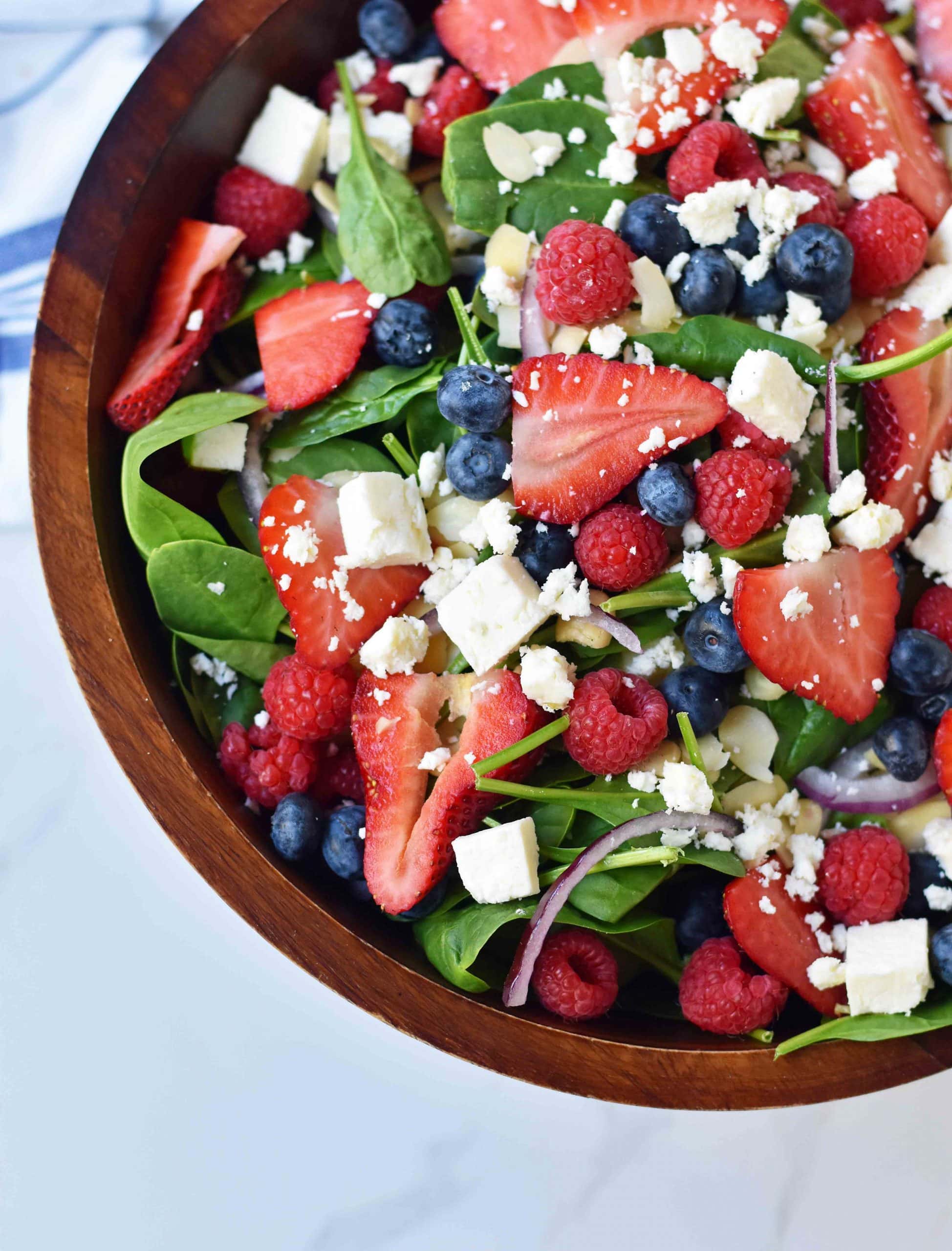 A salad in a wooden bowl full of spinach, fresh berries and feta cheese crumbles.