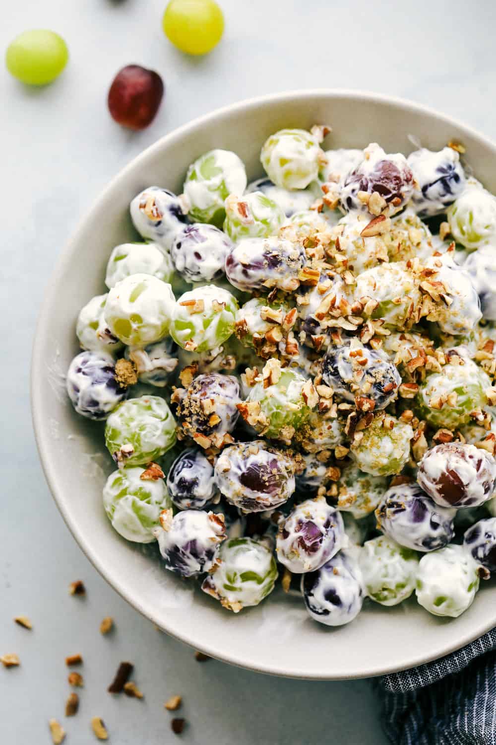 A bowl of green and purple grapes covered in a creamy white sauce, and topped with chopped pecans.