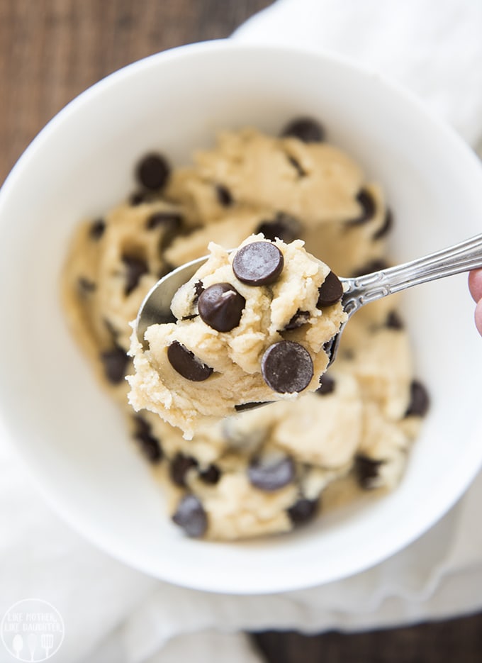 A spoonful of cookie dough topped with chocolate chips, being held above a bowl of cookie dough.