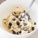 A small bowl full of edible cookie dough with lots of chocolate chips. There is a spoon in the bowl.