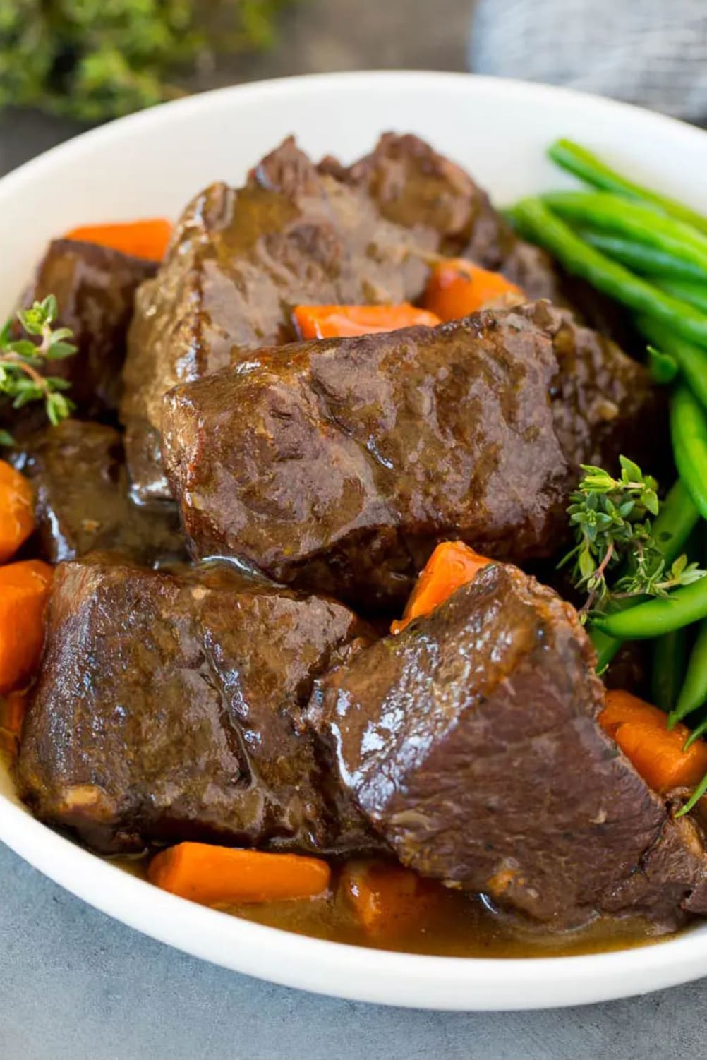 Short ribs covered in a type of gravy on a plate with carrots and green beans.