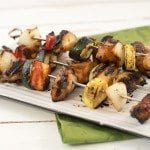 Angled view of teriyaki chicken and vegetable kebabs on a white plate.
