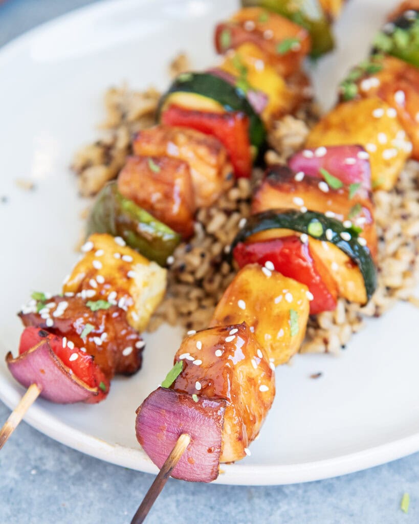 A plate of rice topped with two chicken kabob skewers with chicken, peppers, onion, pineapple, and zucchini.