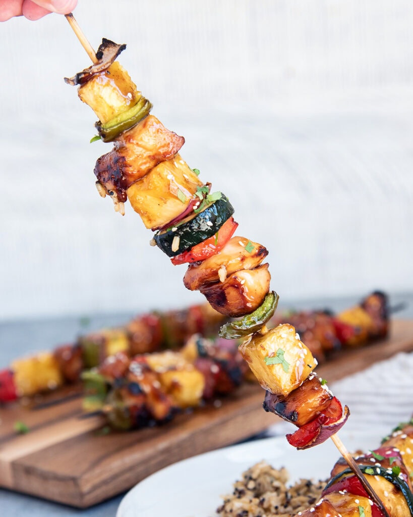 A hand holding a chicken teriyaki kabob loaded with veggies and pineapple.