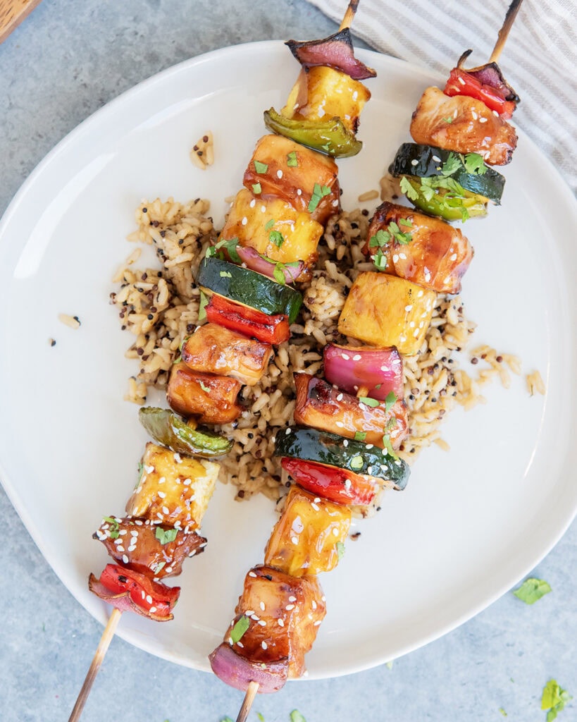 A plate of rice topped with two chicken kabob skewers with chicken, peppers, onion, pineapple, and zucchini.