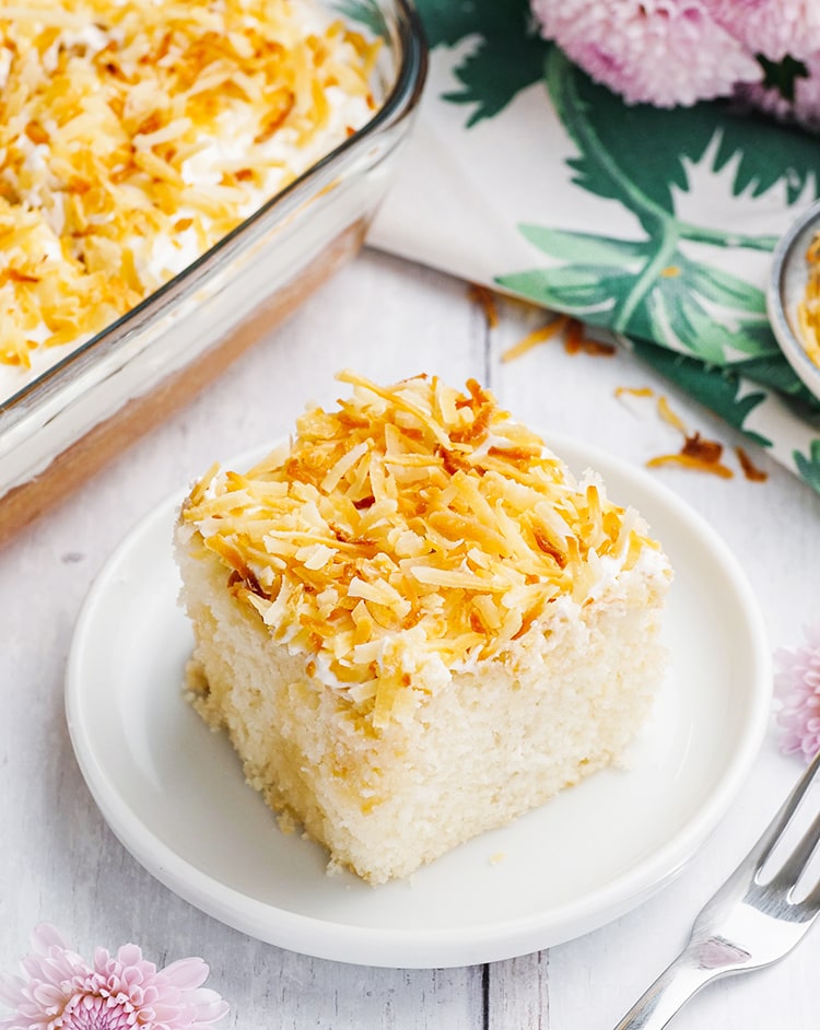A slice of Coconut Poke Cake topped with toasted coconut on a plate.