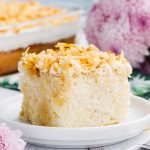 A slice of Coconut Cream Poke Cake topped with toasted coconut on a plate.