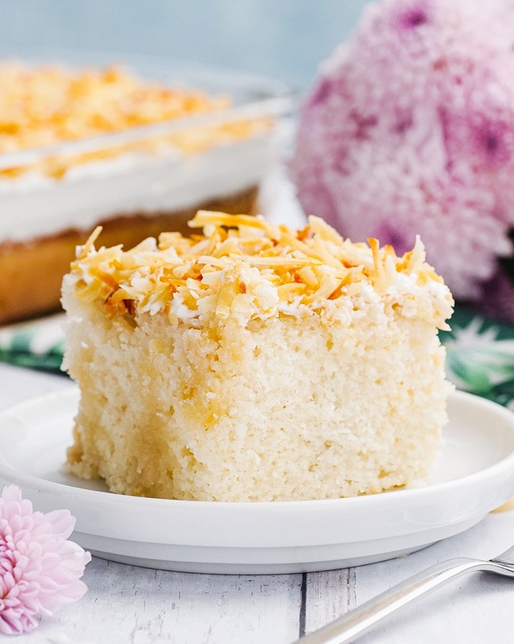 A slice of Coconut Cream Poke Cake topped with toasted coconut on a plate.