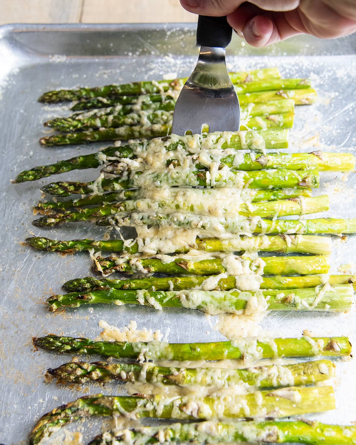 A pan of parmesan asparagus being scooped up with a spatula.
