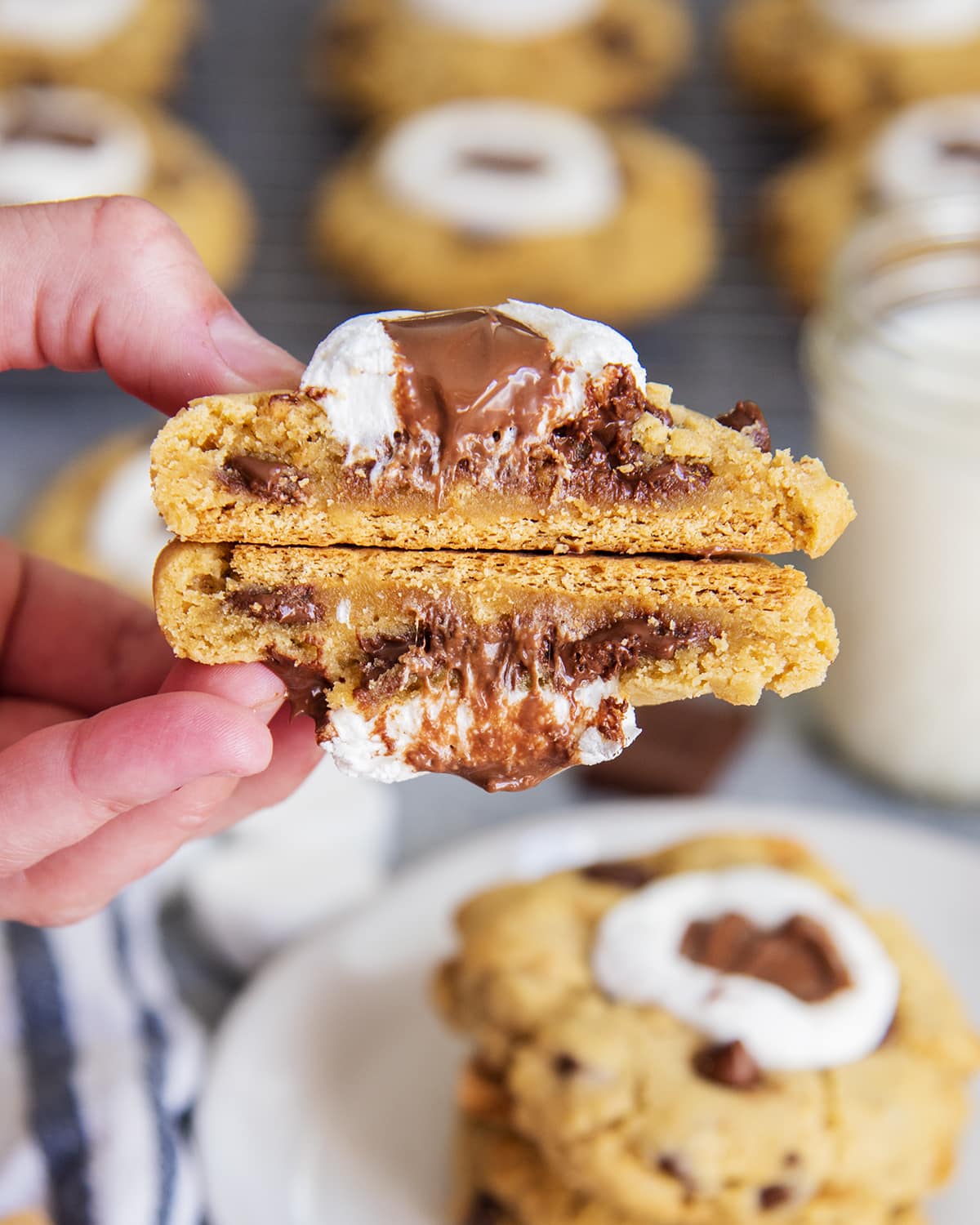 A hand holding two halves of a s'mores cookie showing the gooey inside of the cookie, and graham cracker on the bottom.