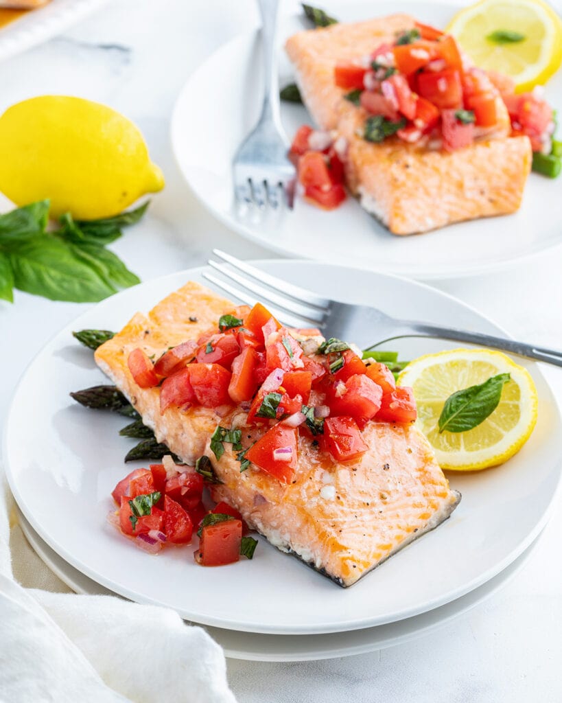 Two plates of tomato basil salmon, with slices of lemon on the plate.