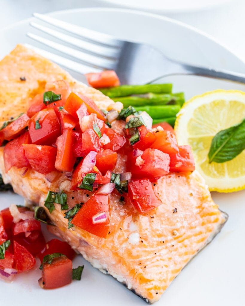 An oven roasted salmon fillet on a plate topped with a fresh tomato basil salsa.