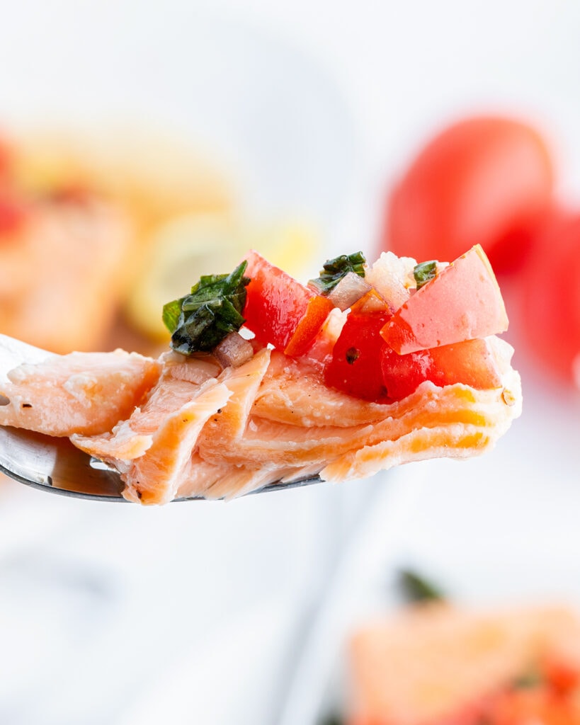 A bite of tomato basil salmon with diced tomatoes on top.