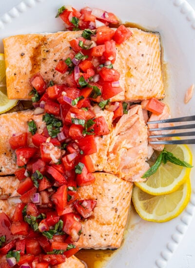 Tomato basil salmon on a platter, with a fork, flaking one piece of salmon into pieces.