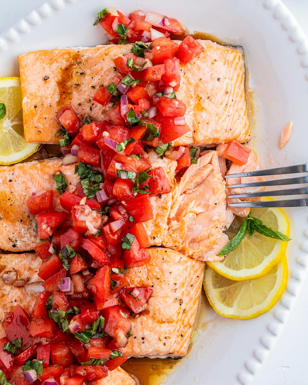 Tomato basil salmon on a platter, with a fork, flaking one piece of salmon into pieces.