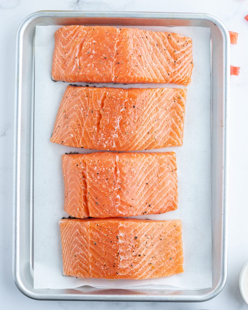 A top view of a baking pan topped with 4 salmon fillets. 