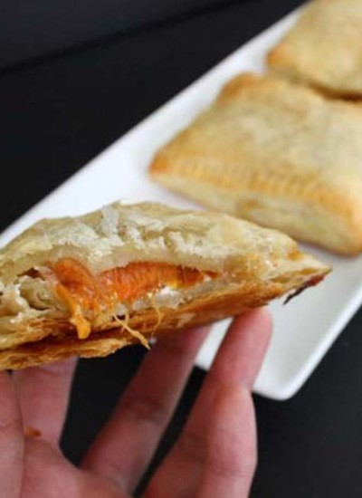 Front view of apricot hand pie in a hand with white plate in the background.