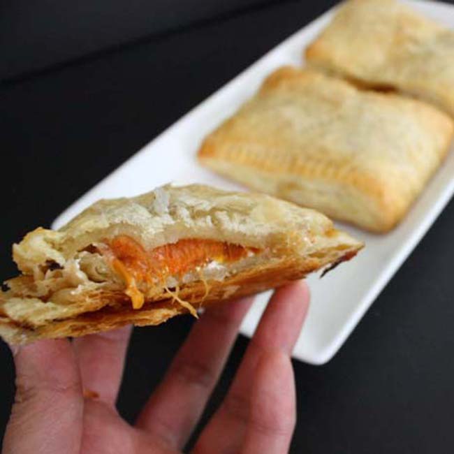 Front view of apricot hand pie in a hand with white plate in the background.