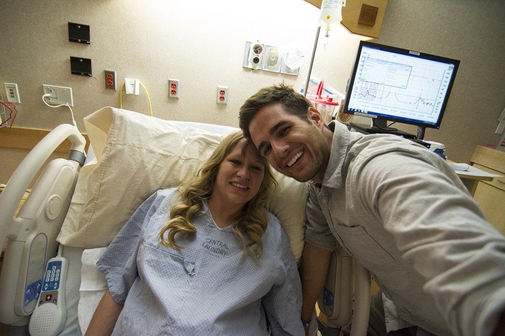 A couple smiles in a hospital as they away a newborn baby.
