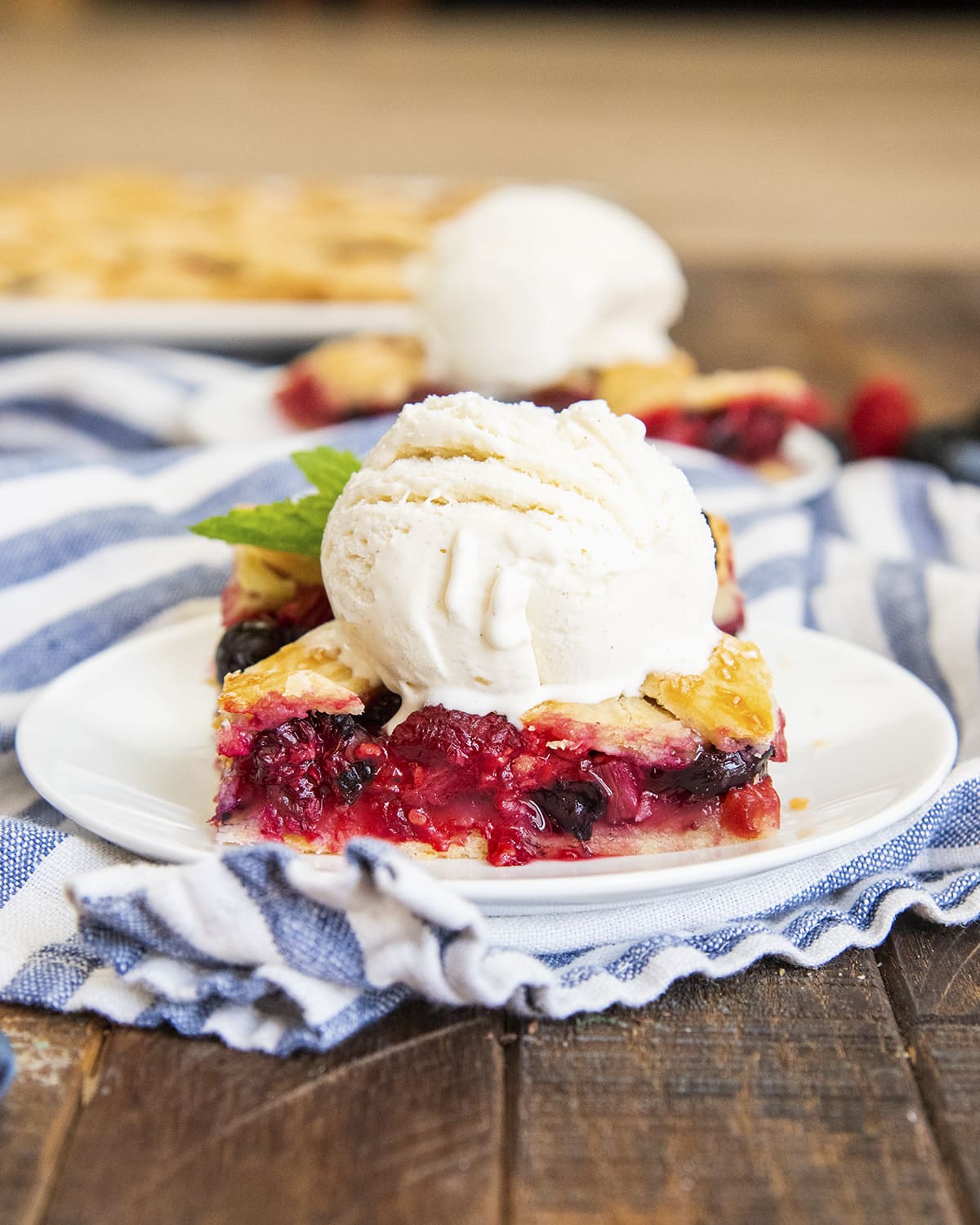 A piece of rhubarb and berry pie on a plate topped with a scoop of vanilla ice cream.