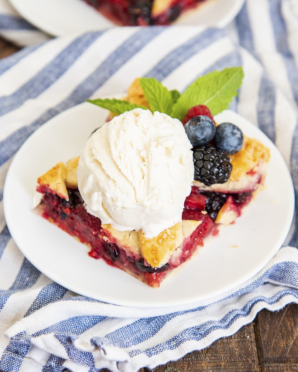 A slice of berry slab pie on a plate topped with a scoop of ice cream.