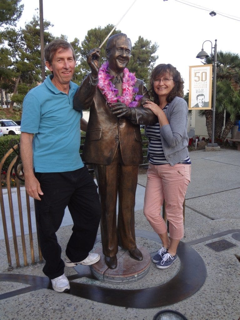 Two people stand in front of a statue smiling.