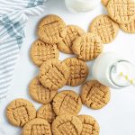Close up image of flourless peanut butter cookies laying next to each other with a glass of milk.